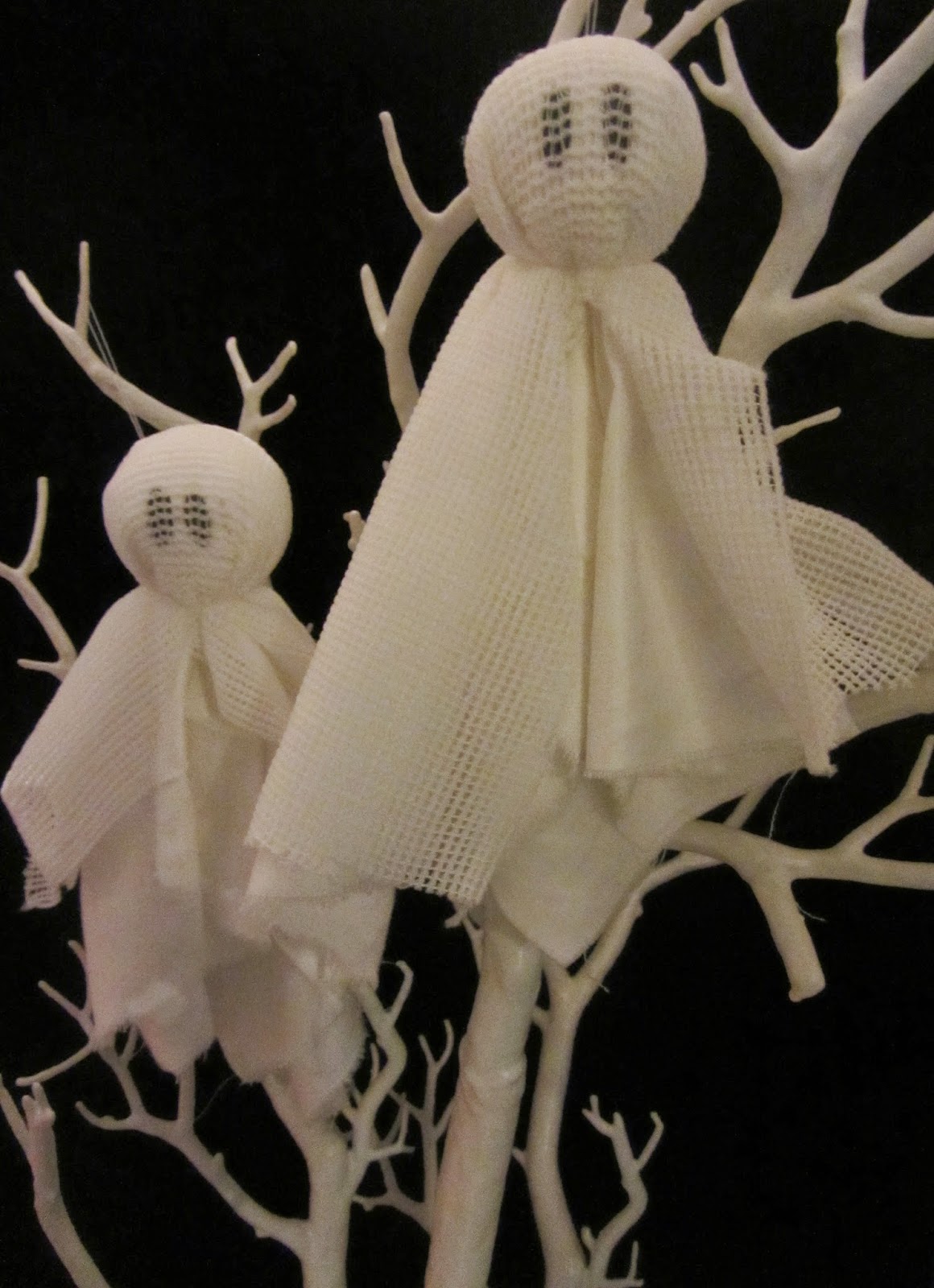 2 ghost decorations hanging on white tree on black background