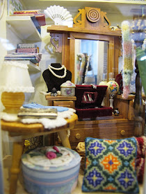 Various items displayed in the window of a one-twelfth scale miniature op shop.