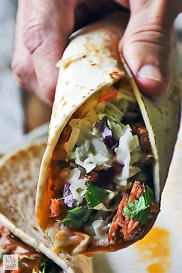 Close up of someone grasping a BBQ Pulled Pork Taco garnished with fresh cilantro ready to take a bite