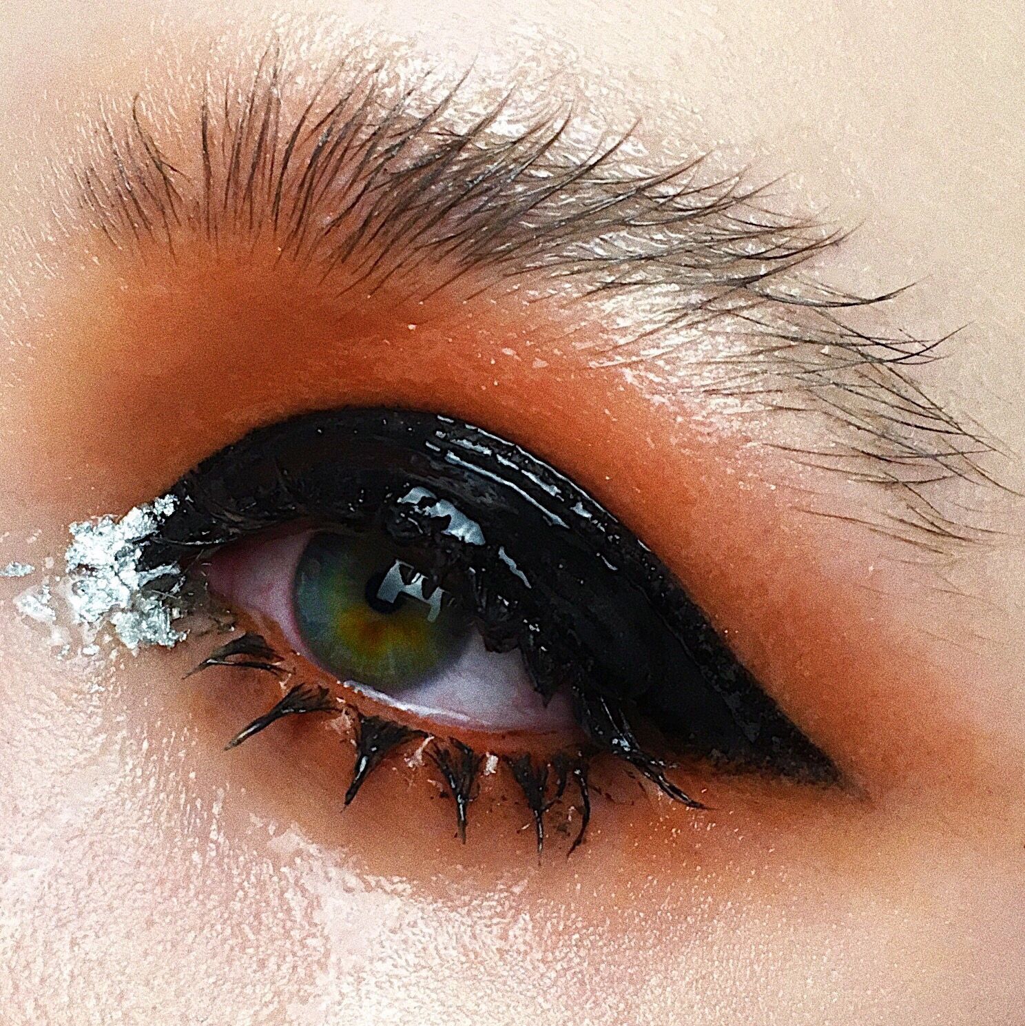 a close-up og a green eye with black and orange glossy eye lid makeup look and fuzzy eyebrows