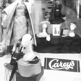 Model of a draper's front window with mannequins displaying frocks and hats. Several signs say 'Carey's'.