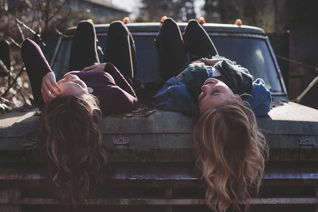 two girls with long hair dangling over car hood