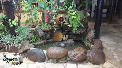 Detalhe do laguinho de carpas com pedra do rio com a bica d'água no pote de barro com a execução do paisagismo e o piso de pedra com cacos de São Tomé.