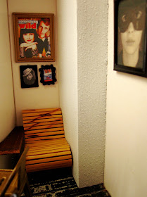 Modern dolls' house miniature cafe corner with a single chair. Above it are a variety of framed pictures of fictional female bandits.