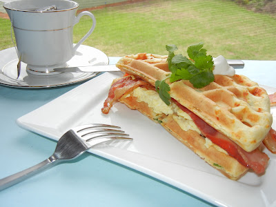 bacon and egg waffle sandwich on a plate with tea in the background and a fork to the left 