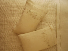 Two dolls' house miniature embroidered pillow cases on pillows, displayed on a white cotton bedspread.