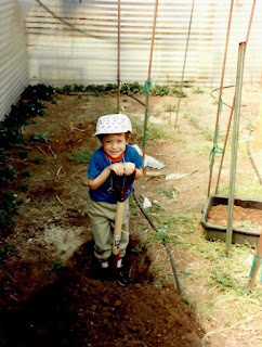 Clayton in the ARBICO garden A young boy in a blue shirt and white hat digging with a shovel in a garden.
