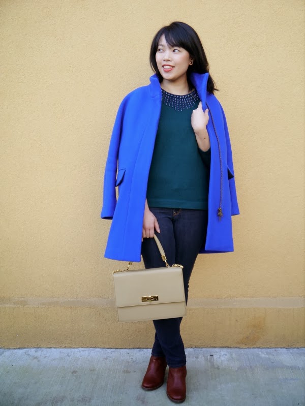 Cobalt blue cocoon coat worn with forest green pullover sweater, dark wash skinny jeans, cognac leather ankle boots, and a taupe top-handle bag.