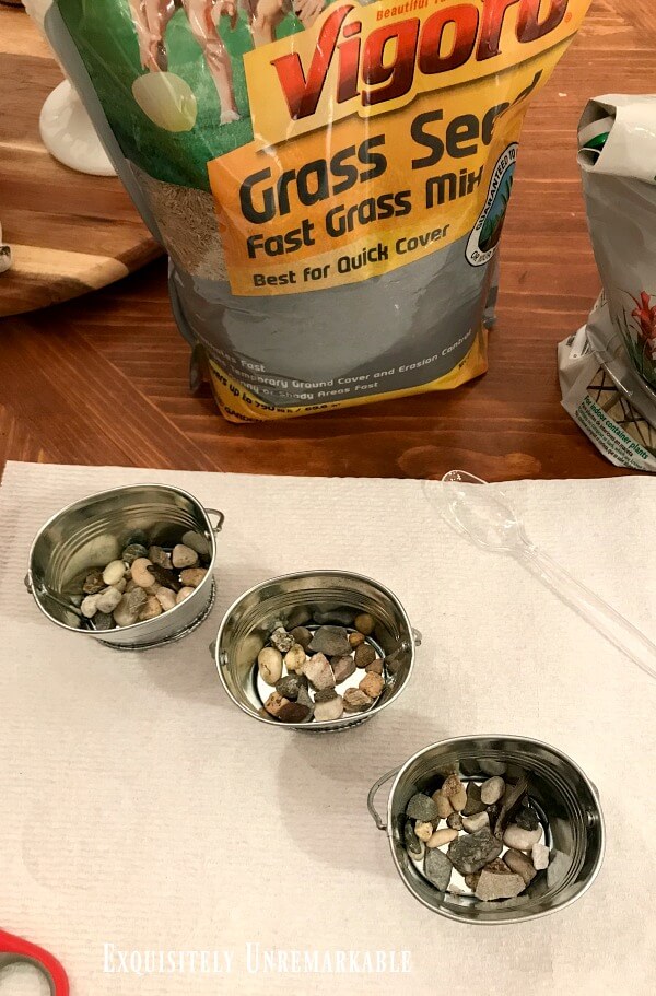 Small tin pots with pebbles in the bottom on each near a bag of grass seed