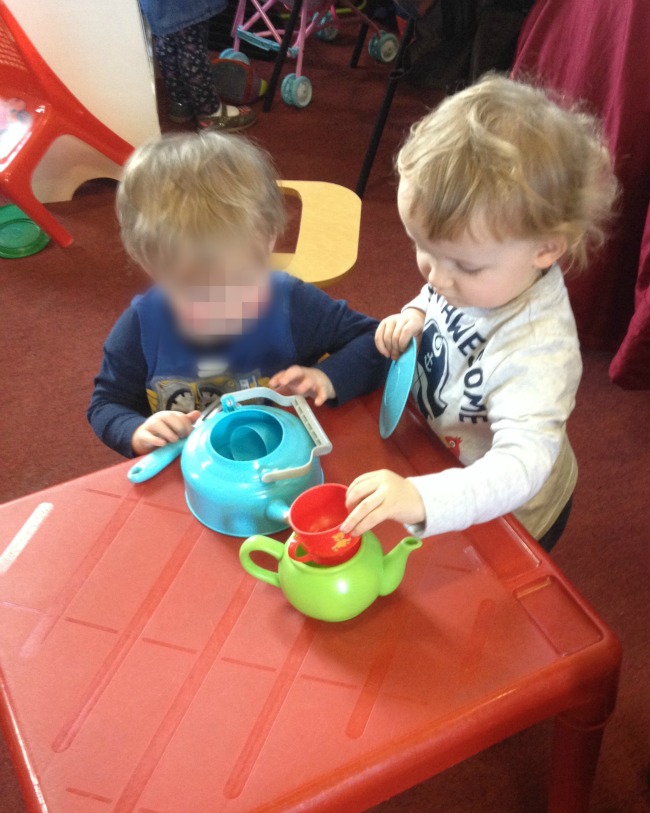 Two toddlers playing with cups and teapots