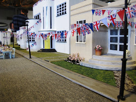 A row of Art Deco houses with british flag bunting strung between the lamp posts and chairs and tables set up for a street party.