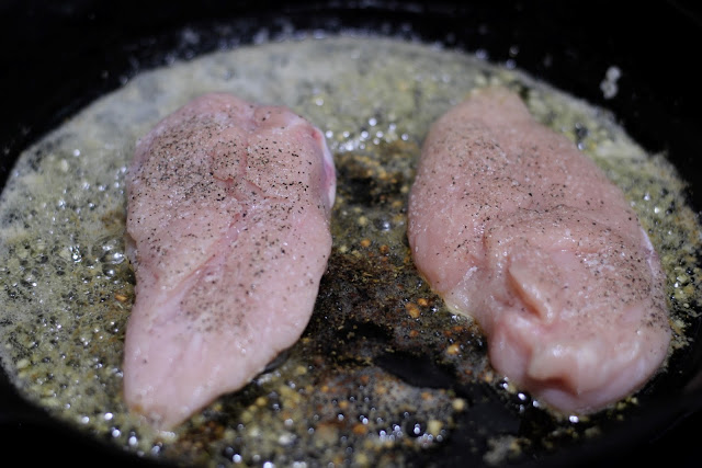The seasoned uncooked chicken breasts being added to the skillet on the stove. 