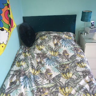A bed with a monkey duvet cover, and a fluffy blue pillow