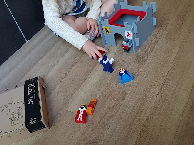 Playing with the wooden castle, the brown cardboard box is also visible