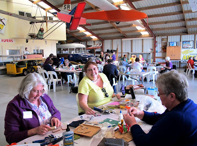 Group of people doing workshops in a hangar. In the middle one woman smiles broadly at the camera.