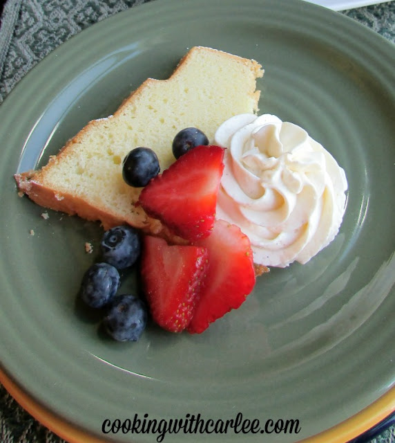 slice of sand torte served with blueberries, strawberries and a piped swirl of cream cheese whipped cream