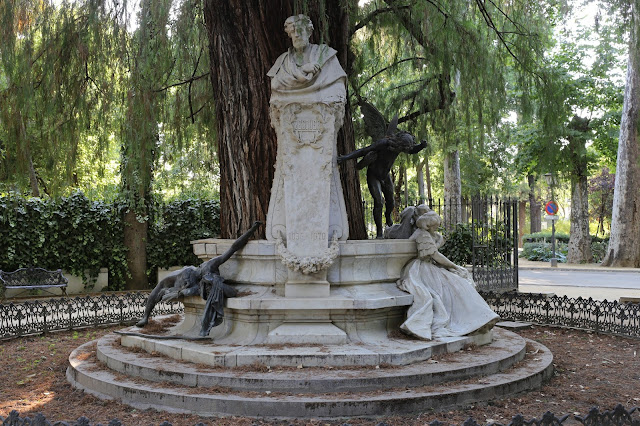 Glorieta entorno a un gran árbol con estatuas en un parque.