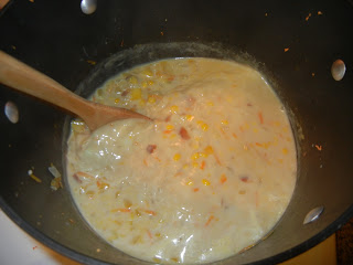 onion, corn, bell pepper, carrots and stock in a pot with a wood spoon to the left 
