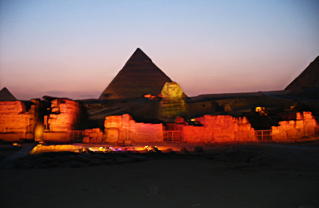 a glowing sphinx and the pyramid at night