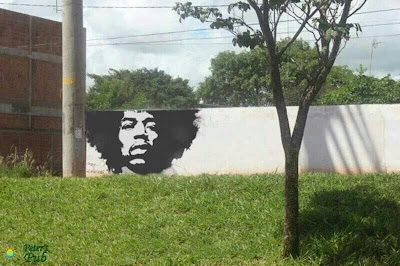 Jimi Hendrix painting on a wall, where the wall ends at top a tree continues his afro