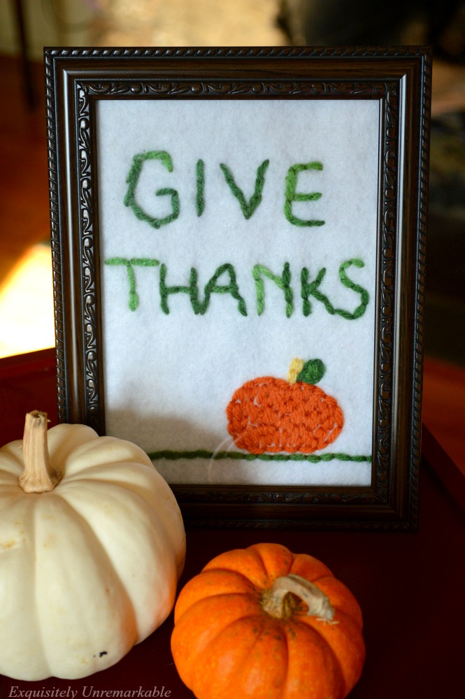 Framed give thanks embroidered design next to two small pumpkins