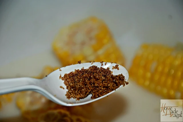 A spoon of brown sugar being added to some coconut milk and spices for boil corn.