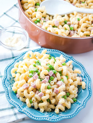 This all in one meal is a delicious combination of ham, pasta, peas and just enough creamy Parmesan cheese sauce. It is a great way to use leftover ham and is sure to have everyone asking for seconds! plate of served pasta with ham and peas in front of pan of remaining pasta