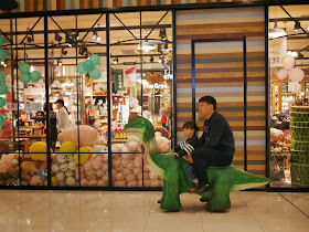 father and daughter riding an electric dinosaur kiddie car at the Mudanjiang Wanda Plaza