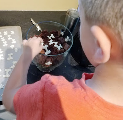 kid placing white chocolate bones between layers of chocolate cake and pudding in glass bowl