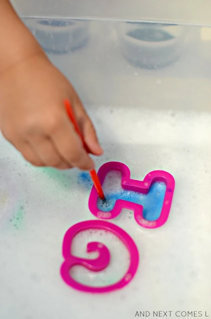 Child painting letters into soap foam using cookie cutters and liquid watercolors