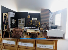 Modern dolls' house miniature room in progress, stuffed with various items of furniture and accessories.