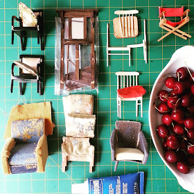 Selection of broken one-twelfth scale miniature chairs (and a hall stand) laid out on a cutting mat with a tube of glue and a bowl of cherries.