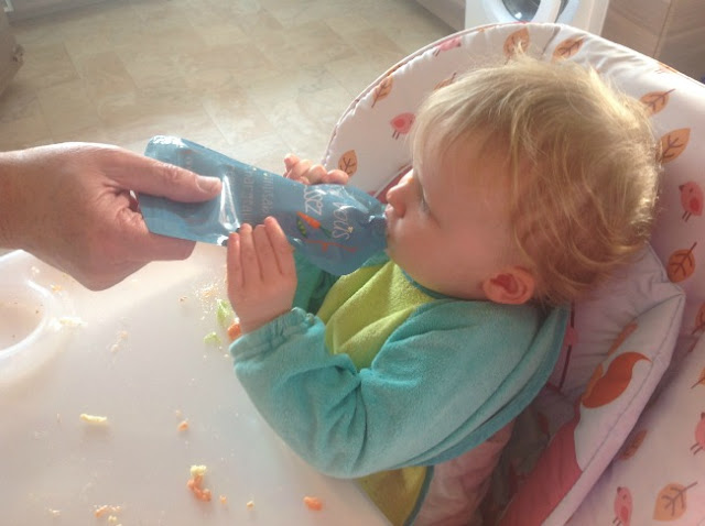 Toddler in high chair feeding from pouch with a hand helping