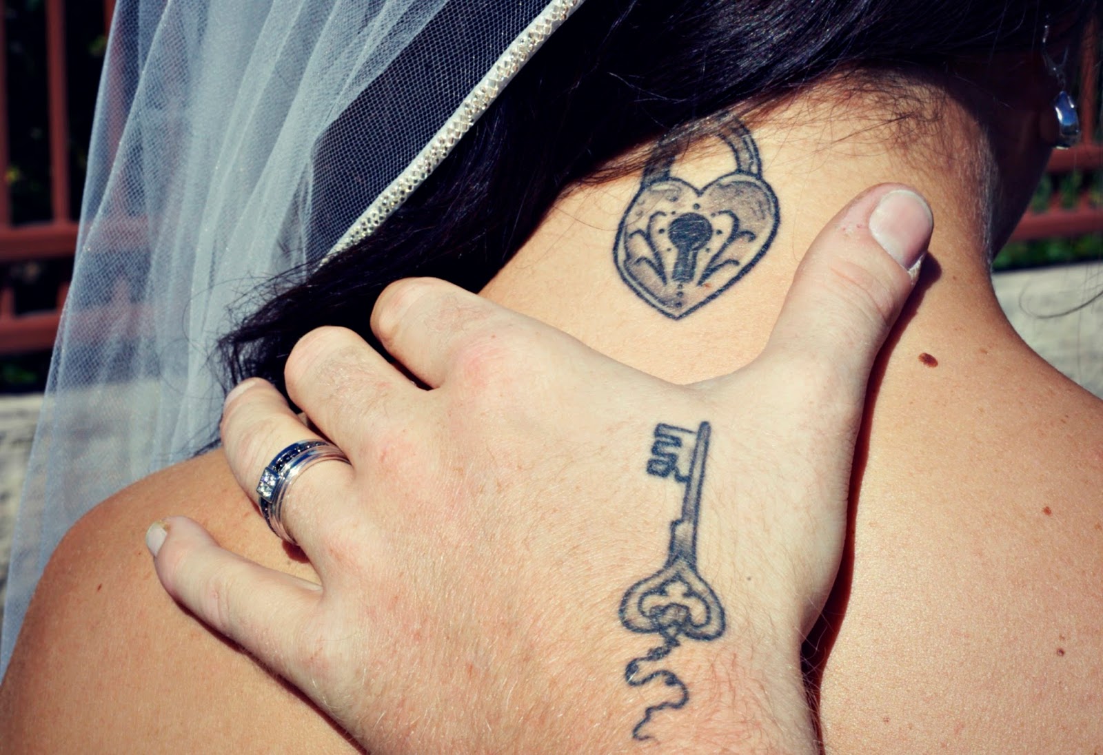 Una pareja de novios, el la acaricia por el cuello, llevan tatuajes de llave y candado, el chico lleva la llave tatuada en la mano, la novia lleva tatuado el candado en la nuca