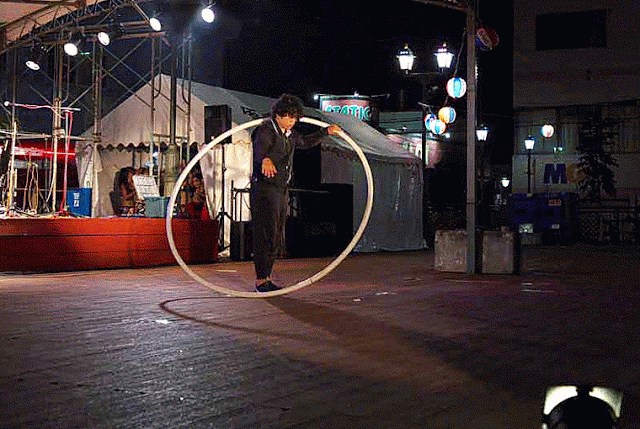 Performer spinning inside a large hoop, night scene, festival