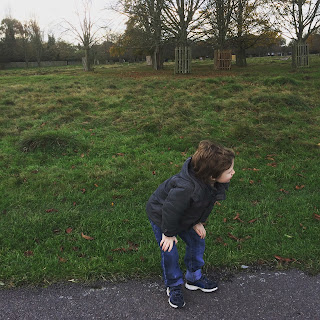 Autistic boy resting on his knees in a green park surrounded by trees and grass and a cloudy sky