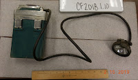 Round electric light connected by black cord to a rectangular battery pack