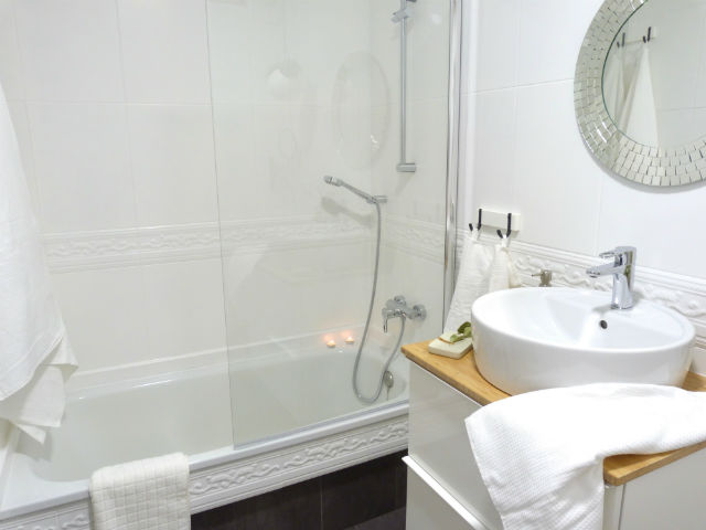 Cómo reformar el baño si obras, detalle de la bañera con el lateral con suelo vinílico y mampara de cristal. 