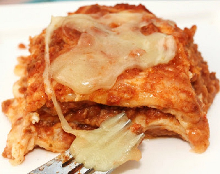 Tortilla layered and filled with melted cheese, meat and refried beans in a casserole dish baked