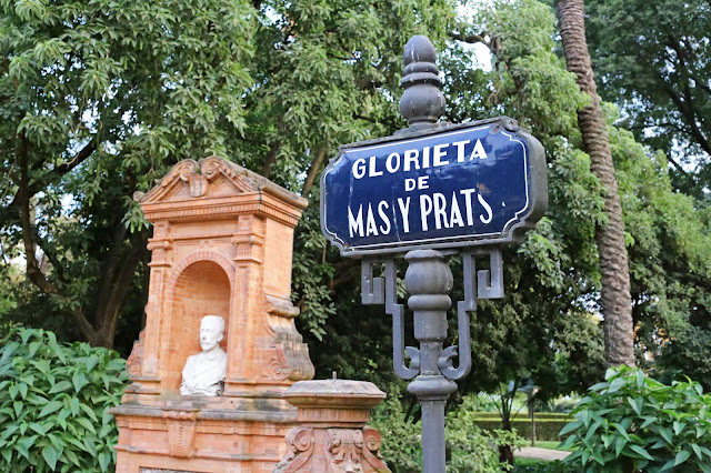 Antiguo letrero con el nombre del monumento y el motivo principal del monumento, en un parque con exuberante vegetación de fondo.