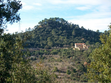 Vista del Mas de Sant Jaume i al seu darrere el Turó del Castell, des del camí de la banda assolellada del Turó de Montgoi