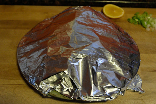 A plate on a cutting board, covered with foil. 
