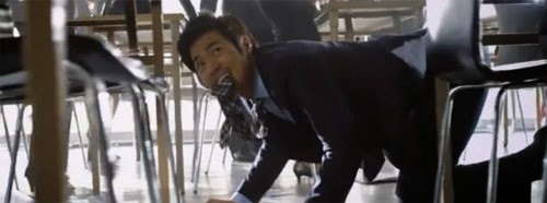 Detective Yang Choon Dong, tie in mouth, crawls through rows of desks.