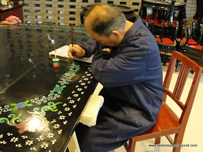 man painting design on laqueur table gift shop at factory reproducing Terracotta Warriors souvenirs in Xi'an, China