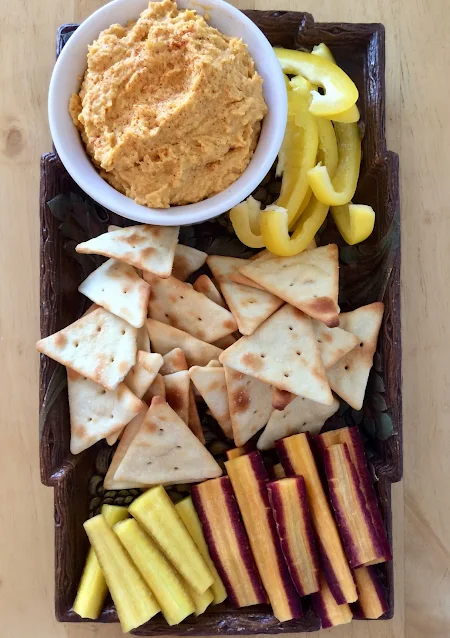 Platter of vegetables and pita chips with a bowl of butternut squash hummus.