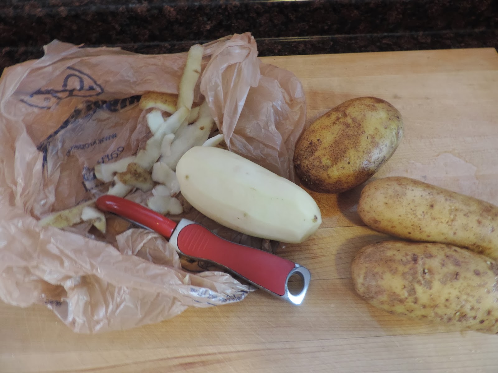 Potatoes getting peeled on a cutting board. 