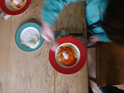 Draufsicht: Kind streut Parmesankäse auf seine Spaghetti