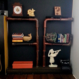 One-tweltfh scale modern miniature pipe shelving mounted on a length of wood, with various miniatures displayed on the shelves and wood surface.