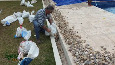 Bizzarri, da Bizzarri Pedras, enchendo a canaleta com pedregulho do rio na cor bege número 2 a 4, sendo canaleta para captar água que cai no piso da piscina em casa em condomínio em Atibaia-SP. 18 de maio de 2017.