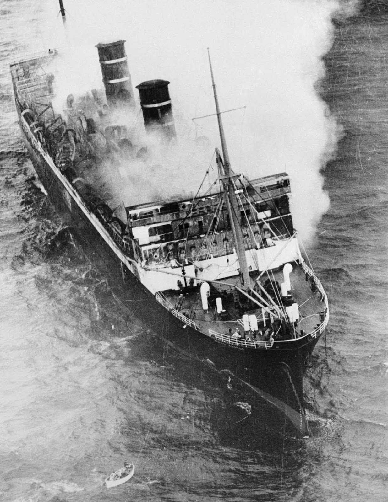 Smoke billows from the burning midsection of the ship as it drifts toward shore.